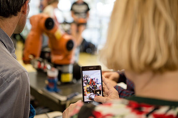 Eine Frau macht ein Handyfoto von einem Roboterarm.