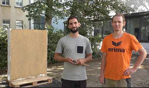 Lehmbau Video zwei Männer stehen vor einer Wand mit Lehmputz