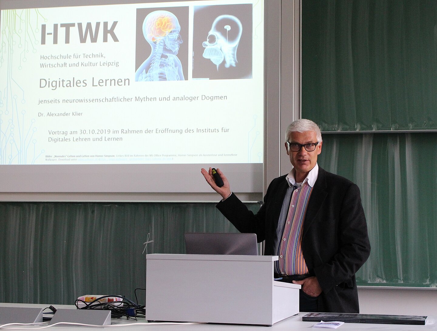Vortrag von Dr. Alexander Klier Person steht am Rednerpult zeigt auf Präsentationsfolien.