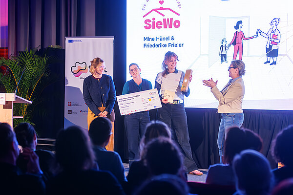 Bei der Preisverleihung nehmen 2 Frauen den Preis entgegen, 2 weitere Frauen stehen auf der Bühne und gratulieren