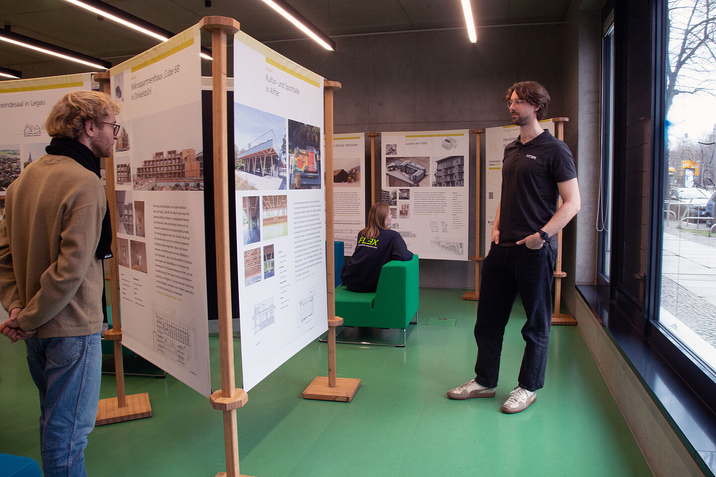 Im Foyer in der Hochschulbibliothek stehen Ausstellungstafeln, Personen besichtigen diese