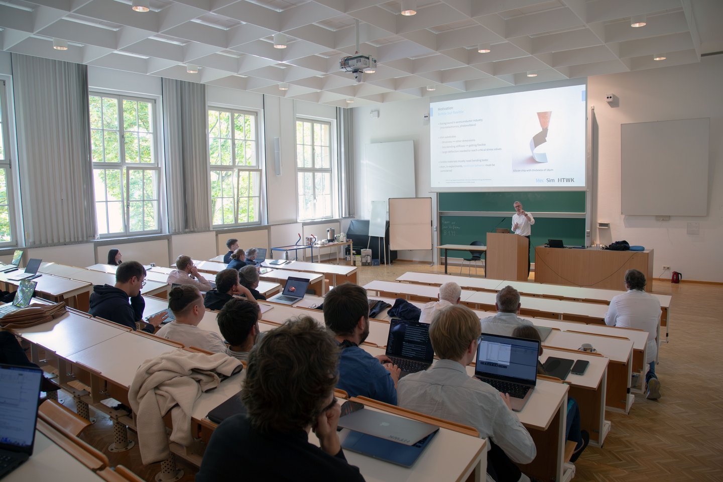 Im Hörsaal sitzen die Teilnehmenden, vorn referiert ein Professor