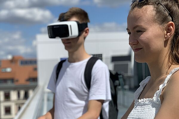 Ein Junge mit VR-Brille und ein Mädchen (jugendlich) auf einem Dach.