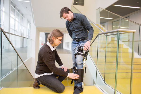 Max has an exoskeleton prototype on his left leg; Felix is adjusting it. (When clicked, the link leads to the project website.)