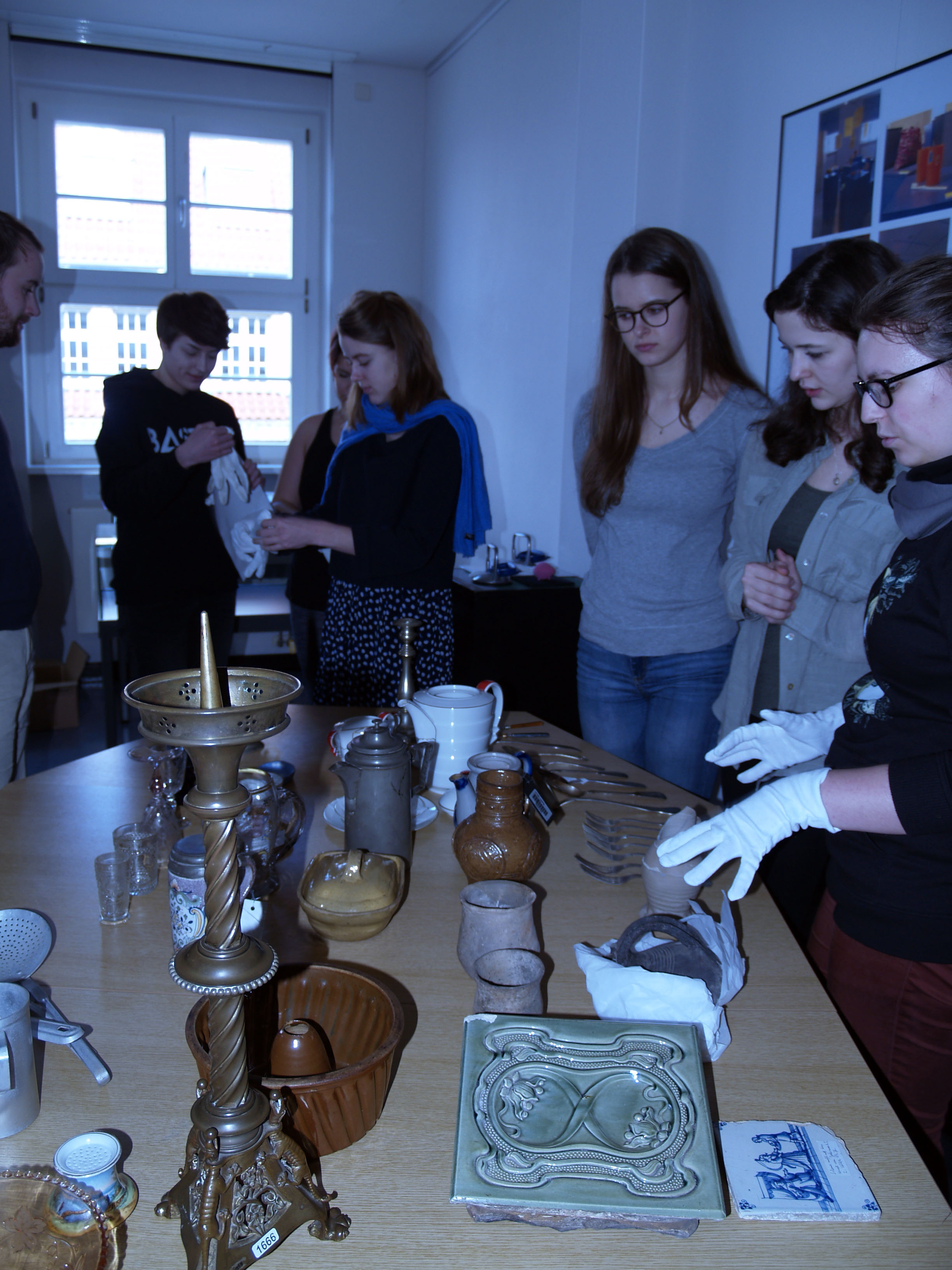 Auf einem Tisch stehen Objekte, dahinter Menschen